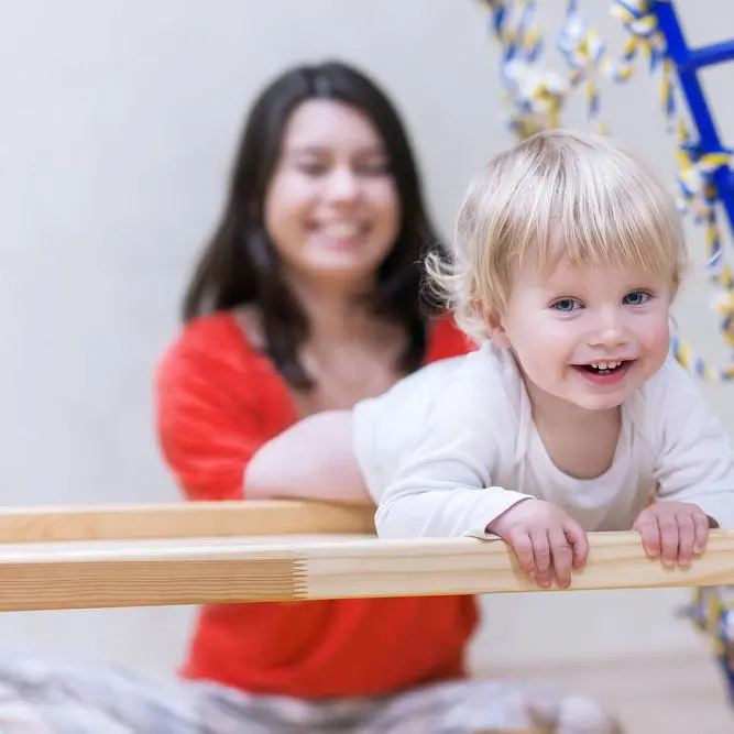 Parent helping their toddler hang from a low beam in a parent and tot gymnastics class